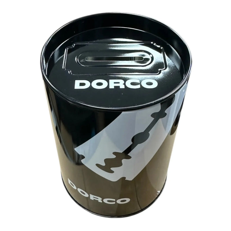 A black metal tin with a slot cutout on the lid, featuring the white DORCO logo and a large white razor blade graphic on the front, photographed on a plain white background.