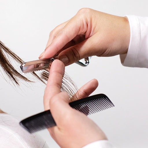 Person using a comb and a metallic styling razor on hair with a white background
