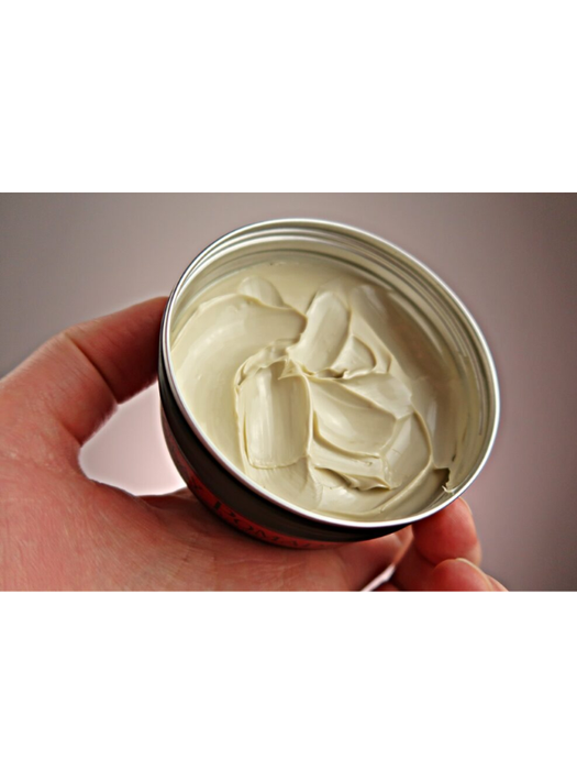 Hand holding a container of white cream against a neutral background