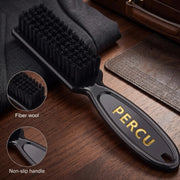 A black grooming brush with black bristles and a black handle featuring gold 'PERCU' branding, shown on a wooden surface with circular inset details highlighting the fiber wool bristles and non-slip handle.