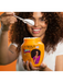 Woman holding a Skala hair care product with a spoon, against an orange background