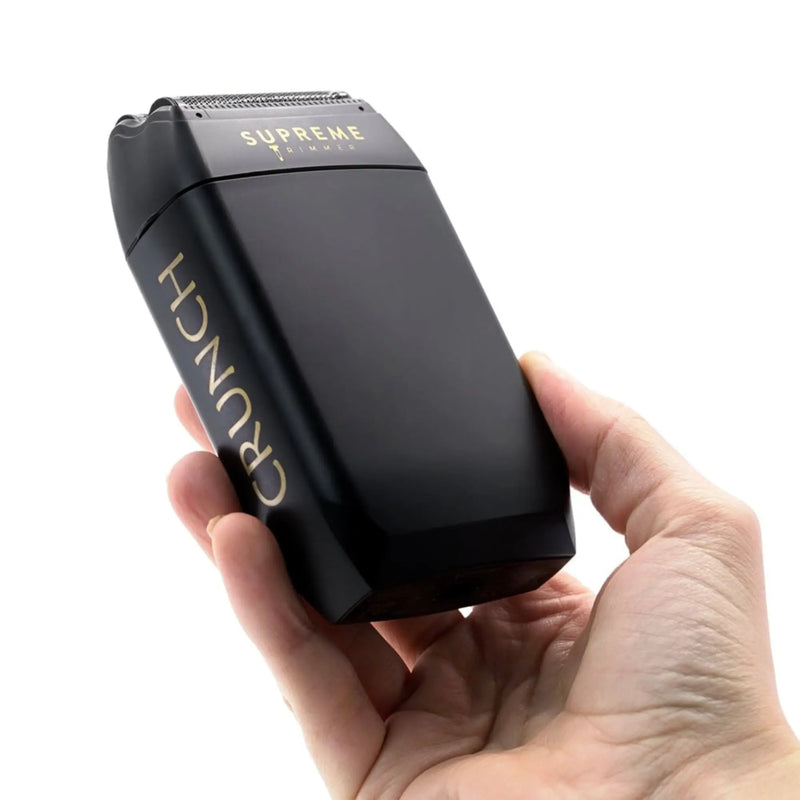 Black electric shaver with 'Supreme' branding held in a hand against a white background