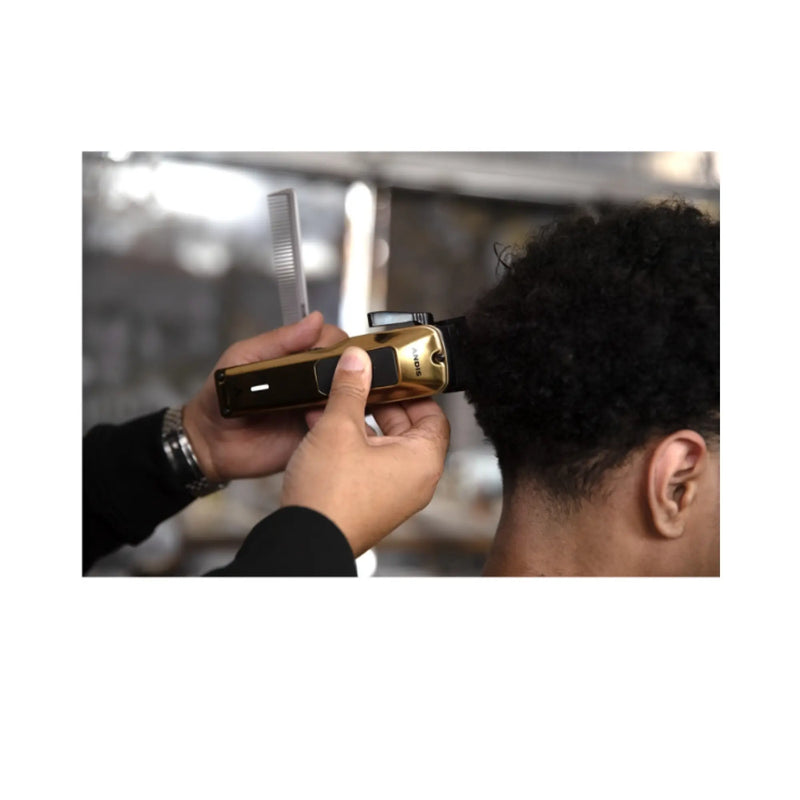 A close-up of a person getting hair trimmed with a black and gold electric clipper, held by a barber's hands, with a comb in hand. The background is a softly blurred salon interior.