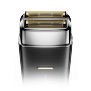 A close-up studio shot of an electric shaver head showing its dual gold-toned rotary blades and polished silver metal collar, set against a clean white background.