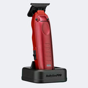 A red BabylissPRO LORPO hair clipper with a black guard attachment, standing on a black charging dock against a light gray background.